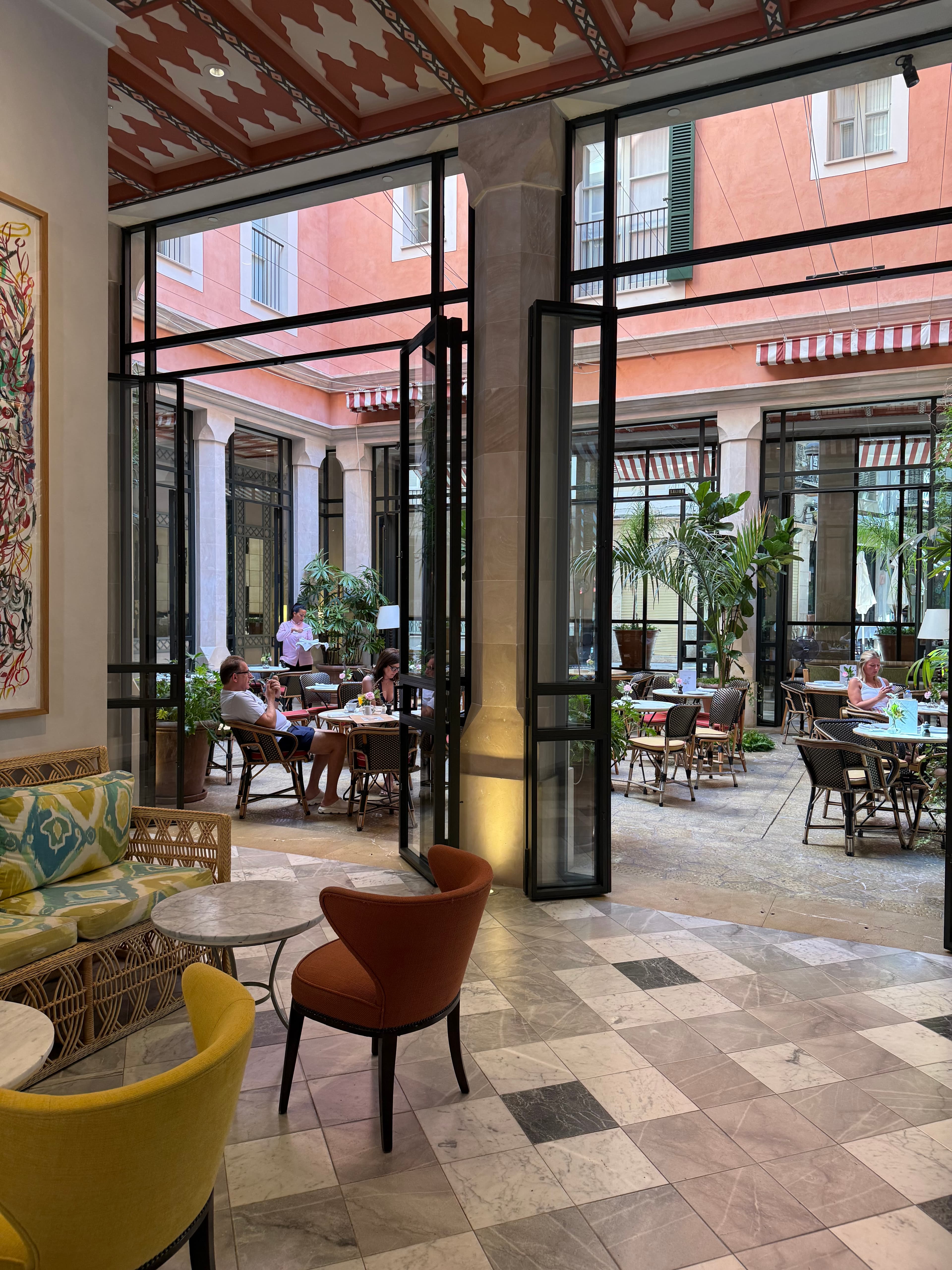 Elegant hotel lobby and glass-enclosed courtyard restaurant with marble checkerboard floors, rattan furniture, and terracotta